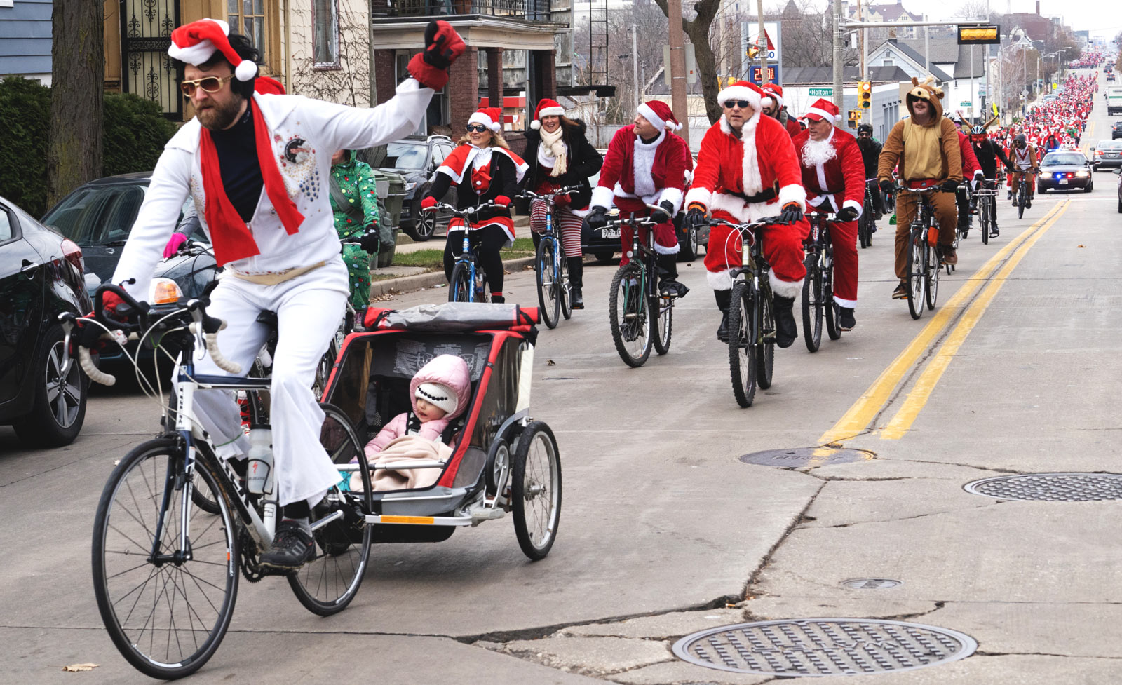 Elvis in a santa hat on a bicycle, followed by thousands of other Santas and other Christmas characters.