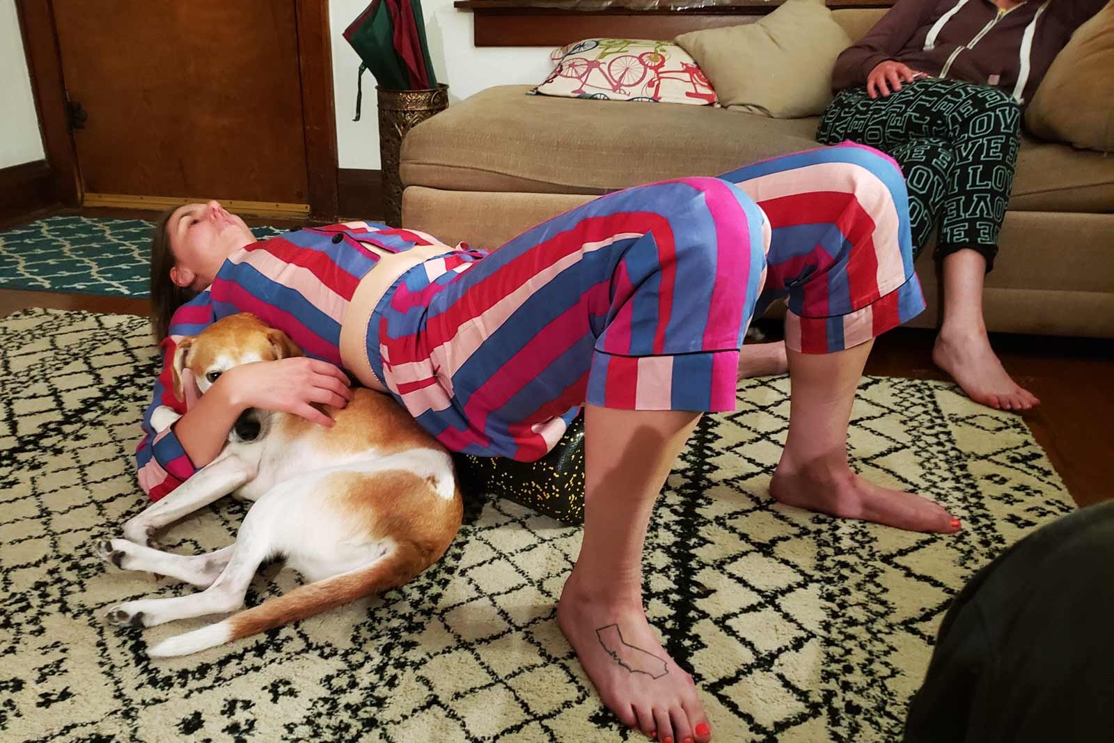 A woman stretches her back and a dog takes advantage.