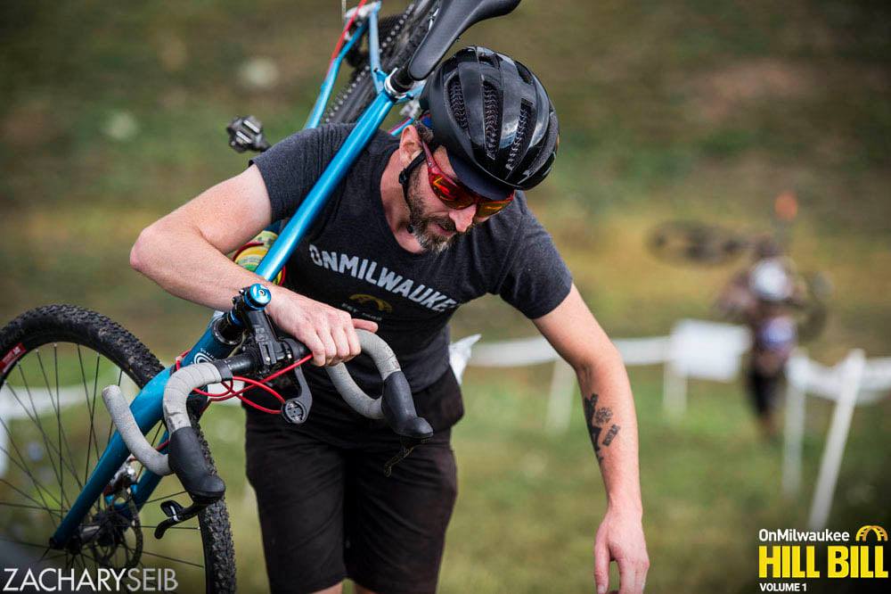 A cyclocross racer dejectedly climbs a steep run-up.