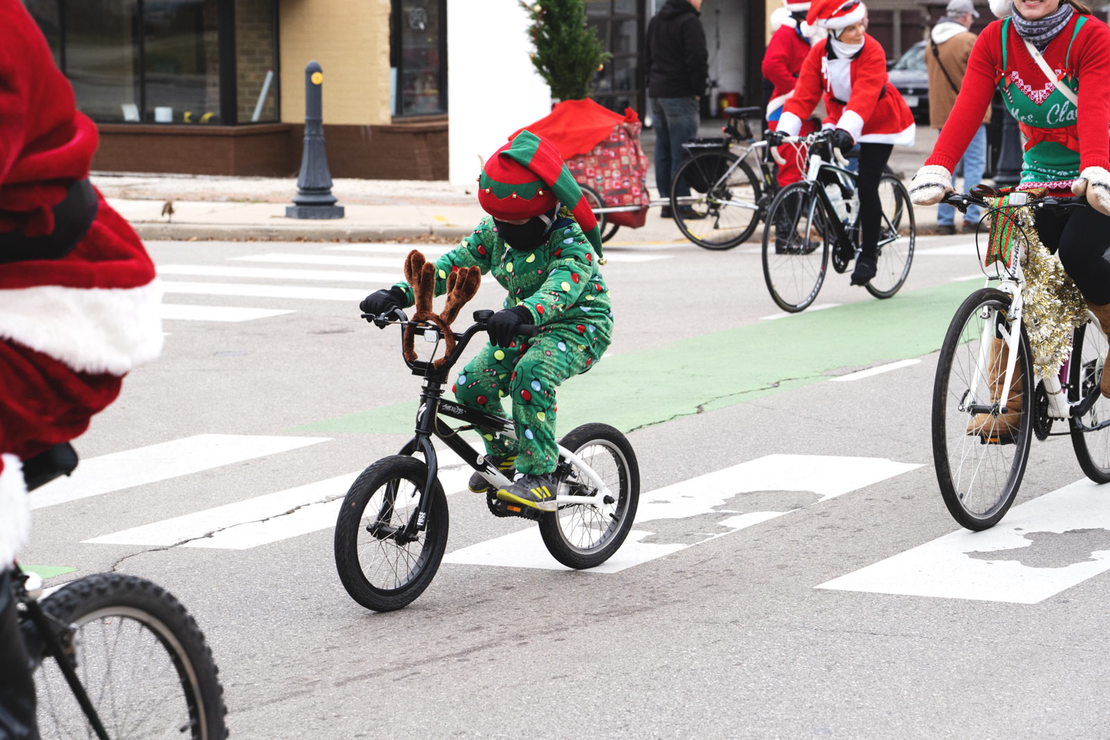 A child in a green christmas light costume on a bike with reindeer antlers.