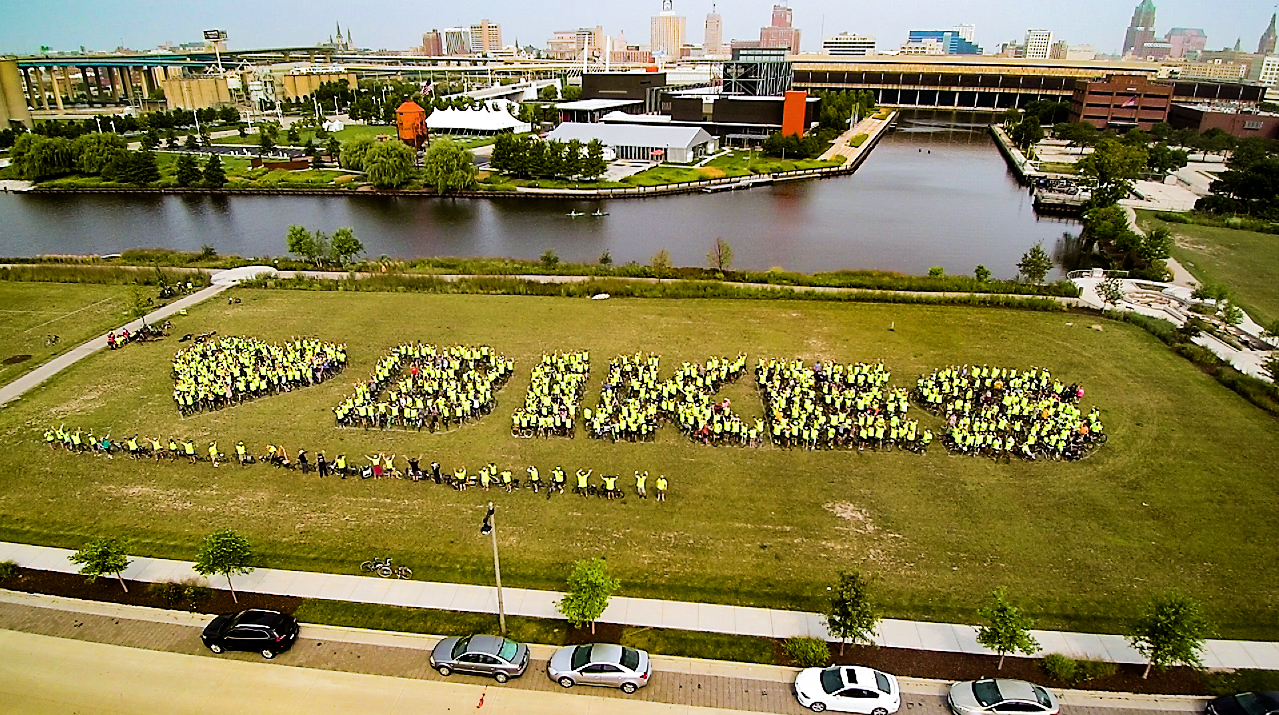 A group of cyclists in hi-viz t-shirts gather together to spell out (Heart) Bikes