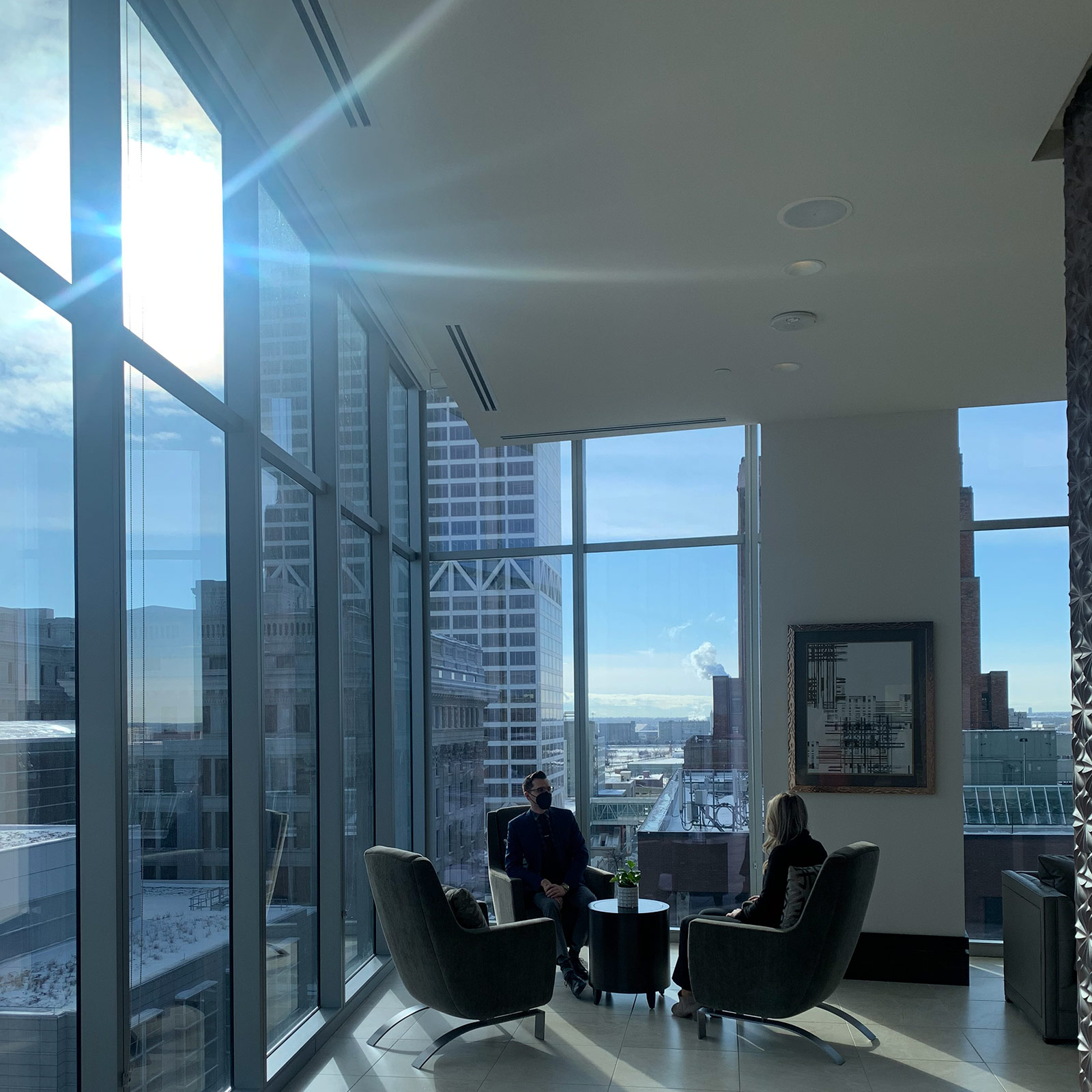 Two residents sit near wall-to-ceiling windows in the common area of the 7SEVENTY7 apartment building.