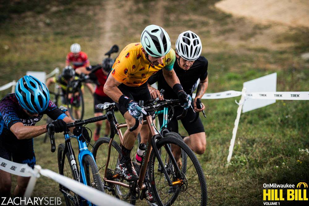 A cyclocross racer rides a steep run-up between two others pushing their bikes.