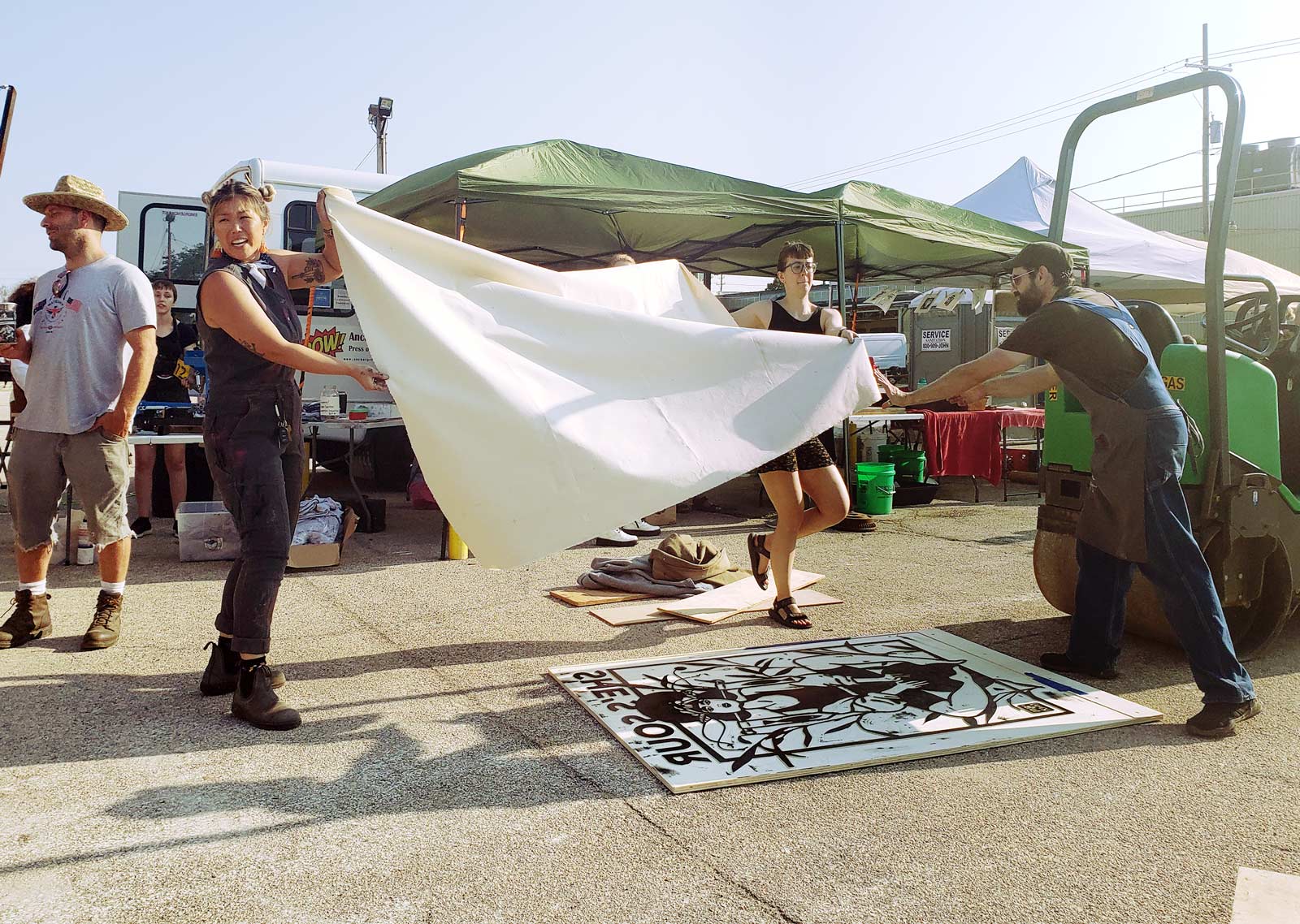 A group of artists preparing to drop cloth onto large woodcut on the ground.