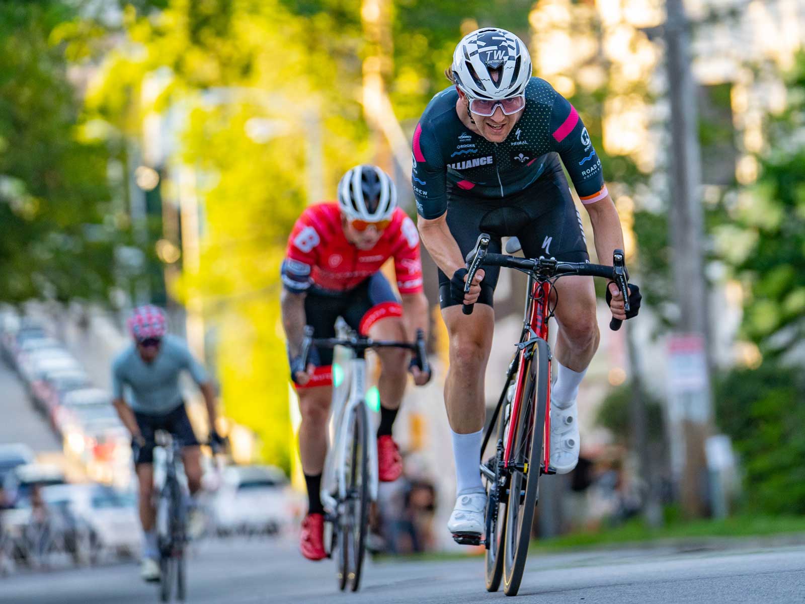 A man charges up a hill on a bicycle, tailed by two others during a crit race.