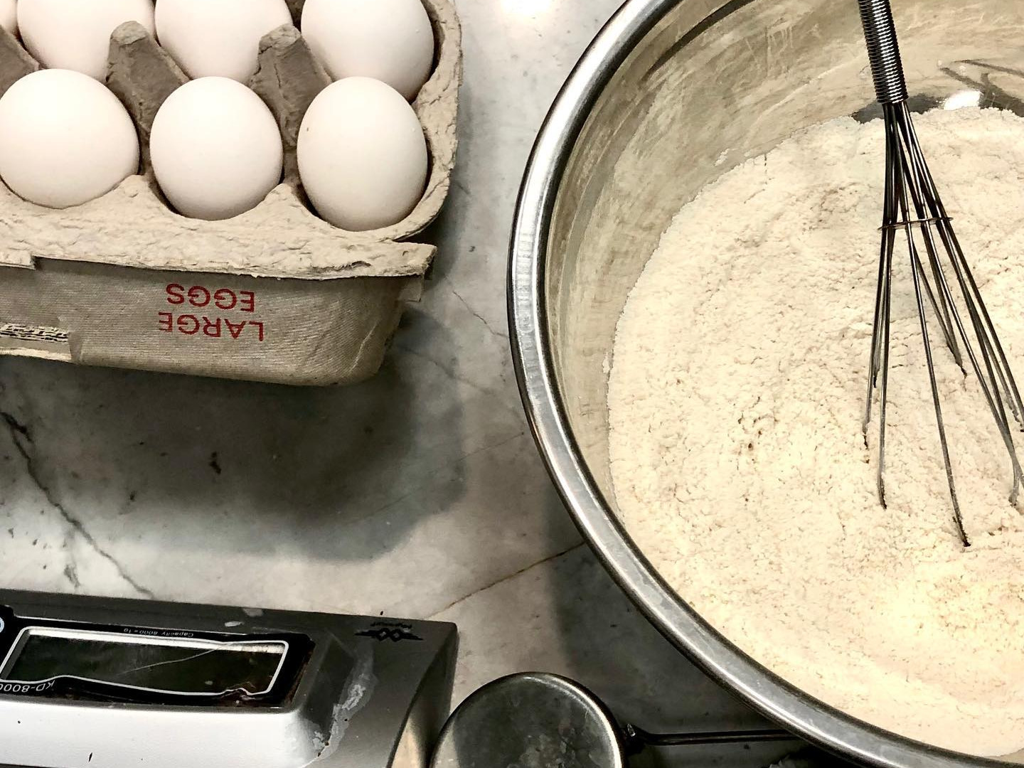 Baking supplies including eggs, flour, bowl and whisk