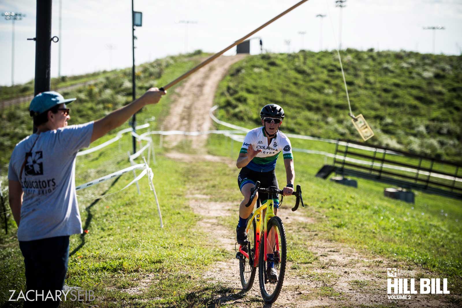 A cyclocross racer reaching out to grab money off of a fishing line.