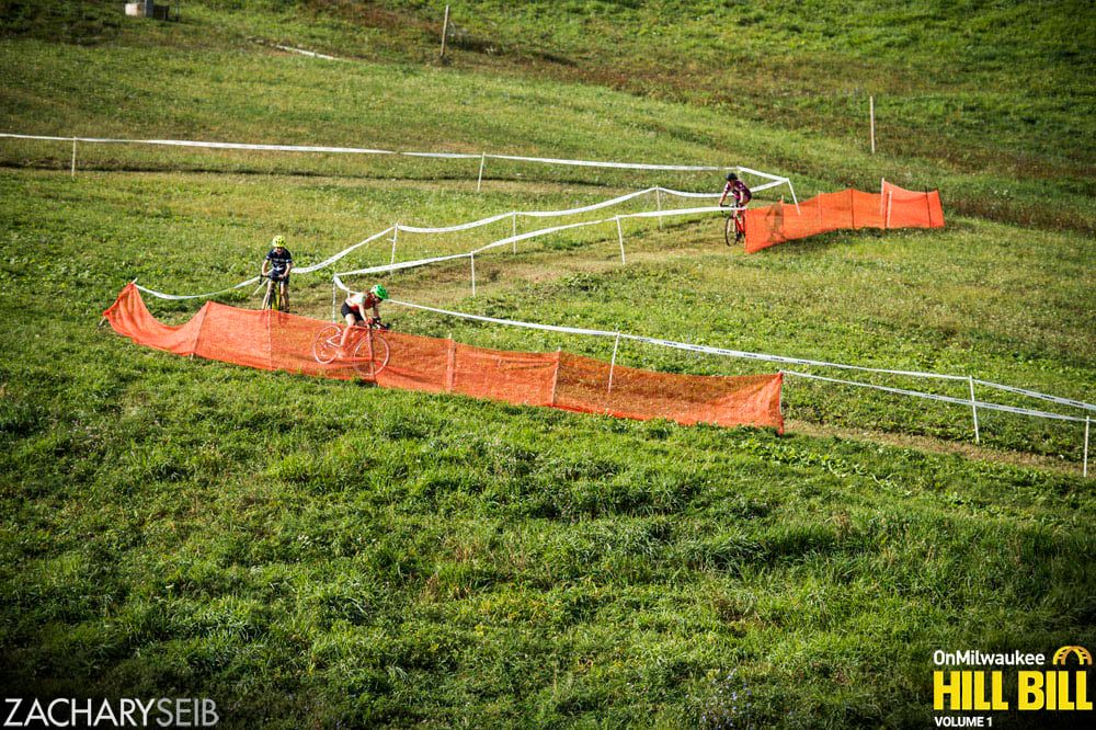 Three cyclocross racers descend a switchback on a snowless ski hill.