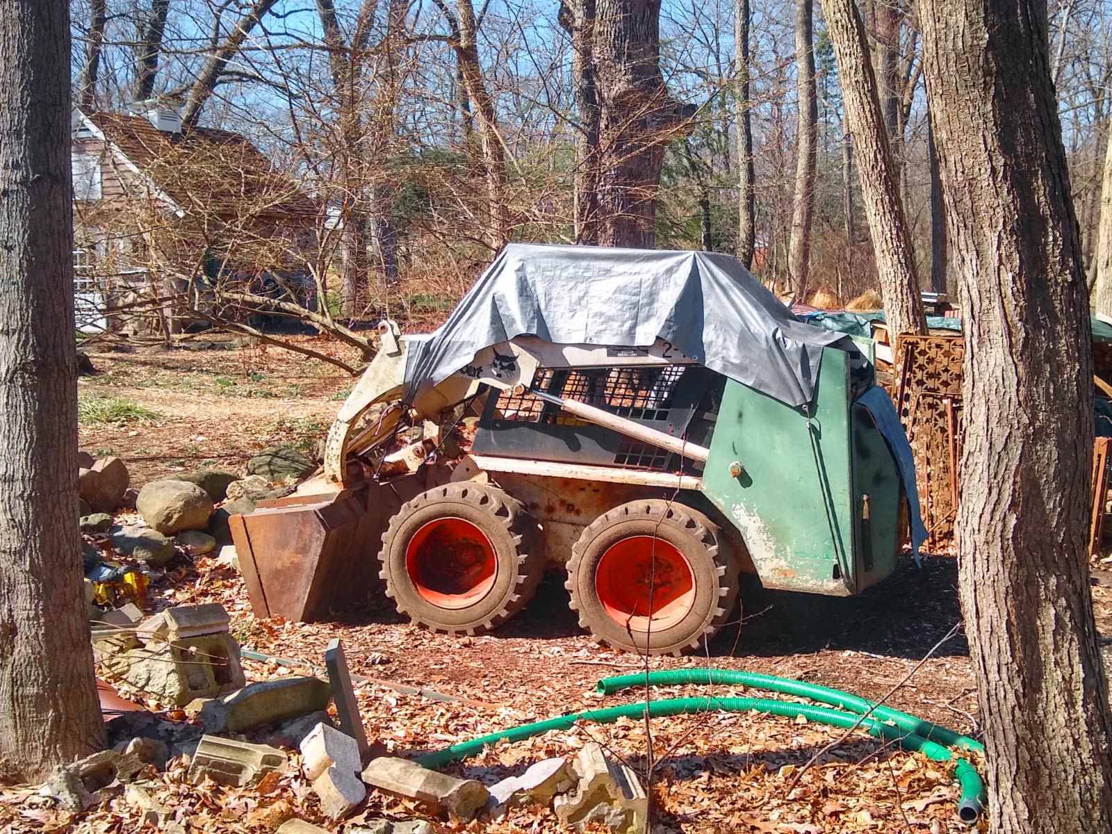 A small back hoe under a storage tarp on public trails.