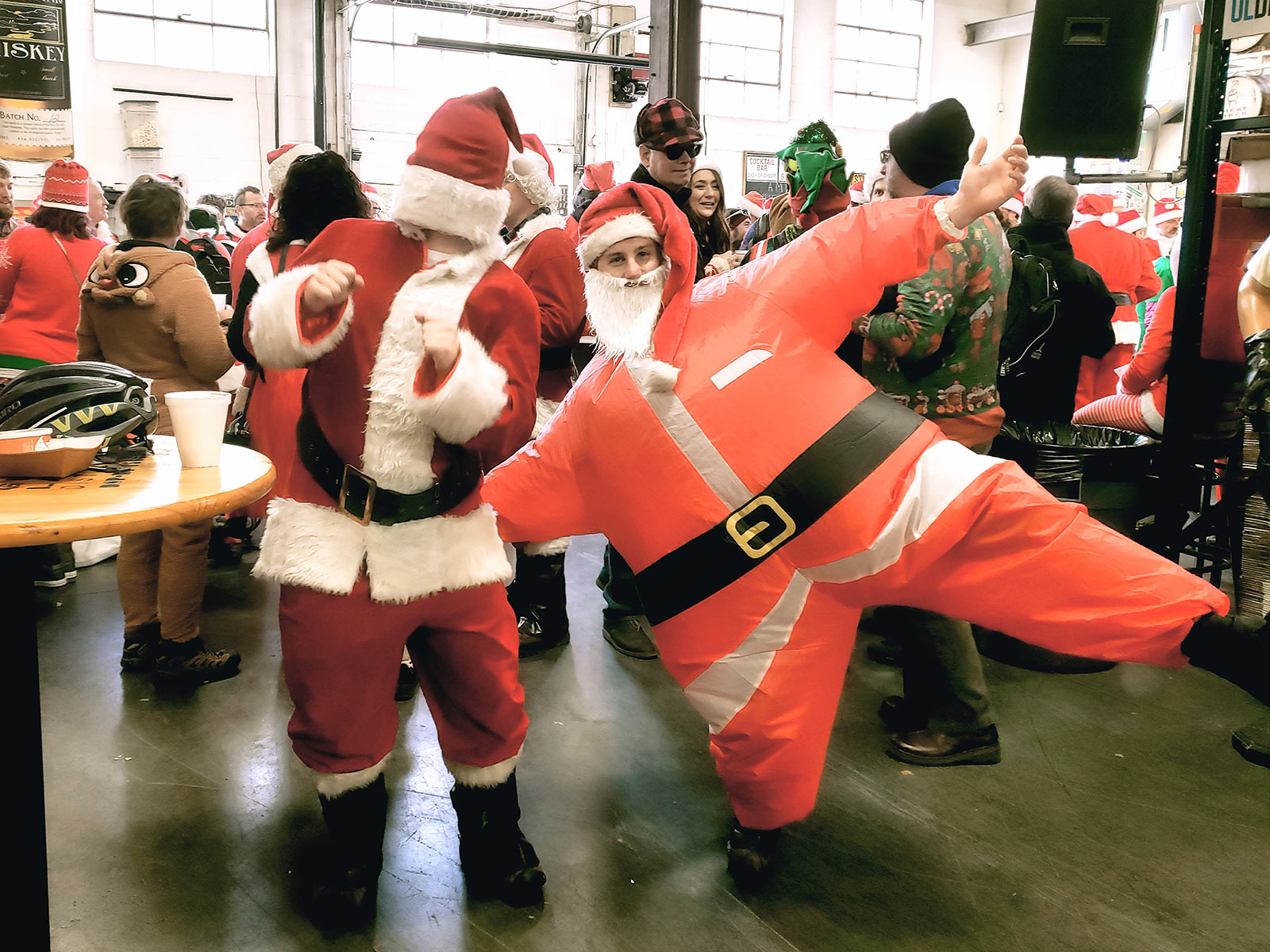 A Santa dancing next to a person in an air-filled Santa costume at Great Lakes Distillery.