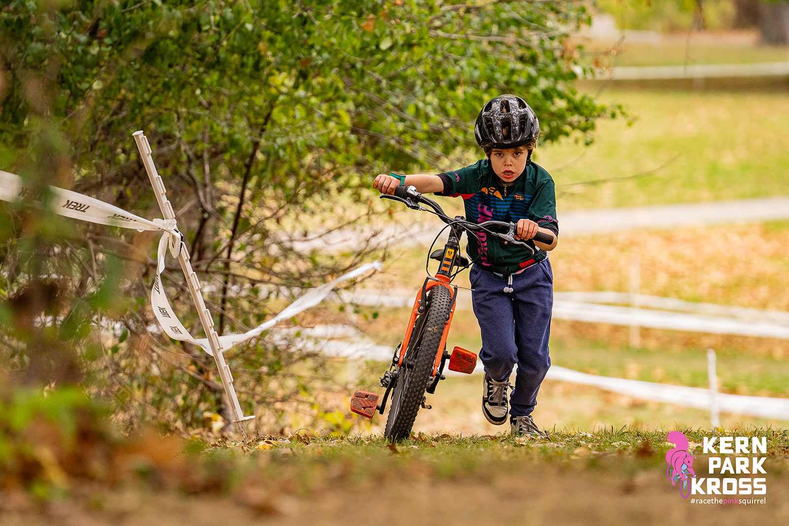 A boy pushes a mountain bike up a hill, surrounded by fall colors.