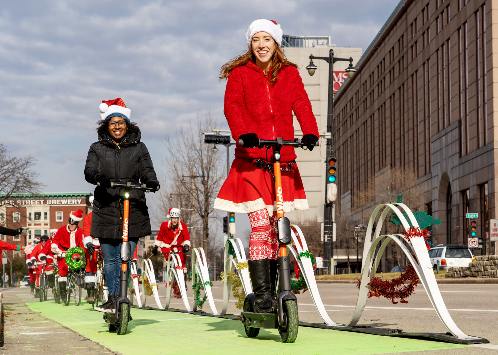 Two women on scooters in Christmas outfits.