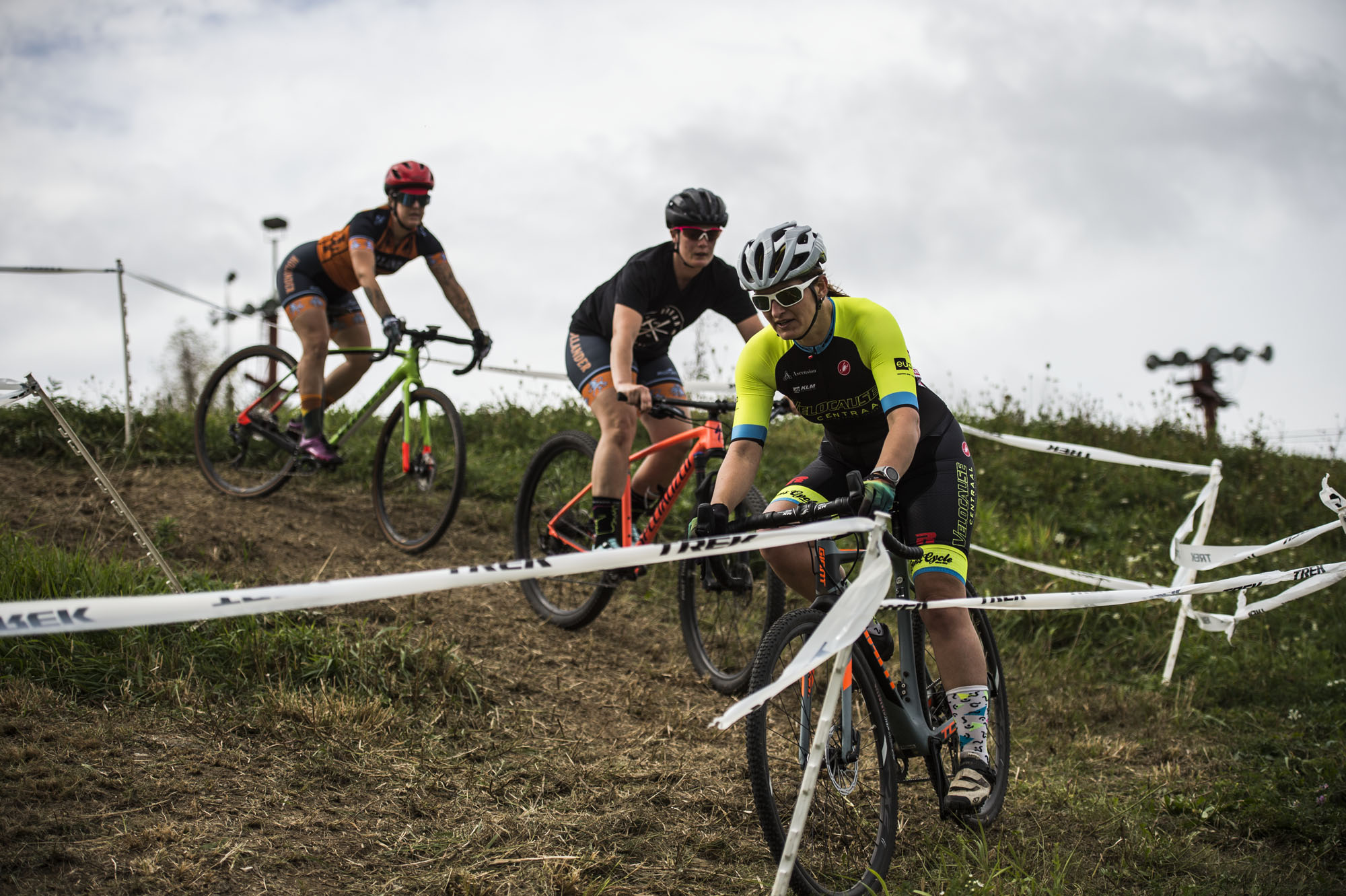 Three cyclocross racers navigate an off-camber switchback.