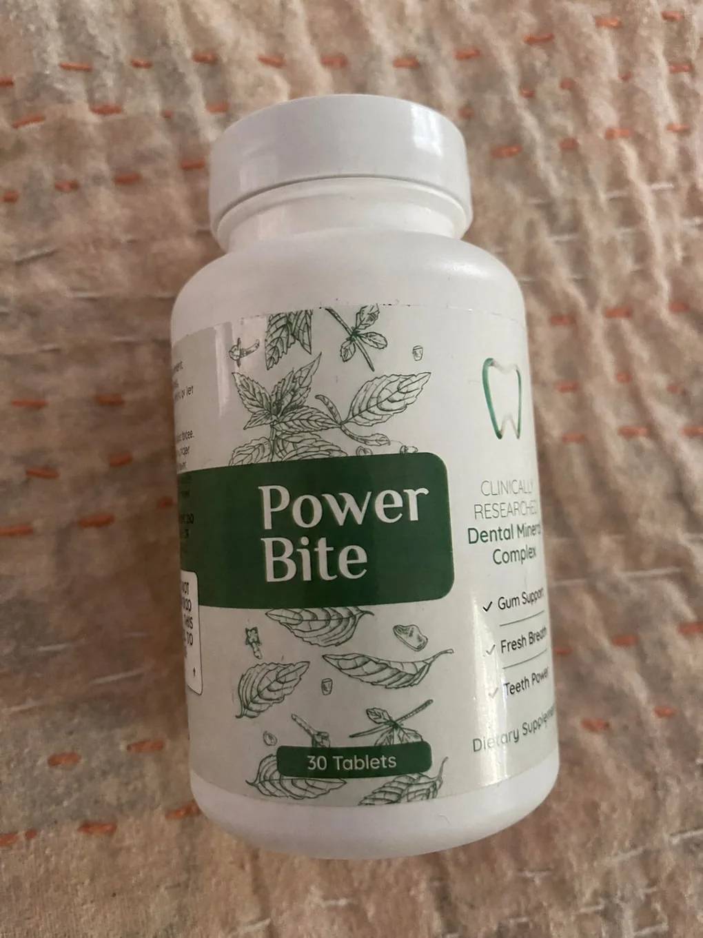 PowerBite bottle upright on a pink cloth, green-and-white label reading Power Bite Dental Mineral Complex, 30 Tablets