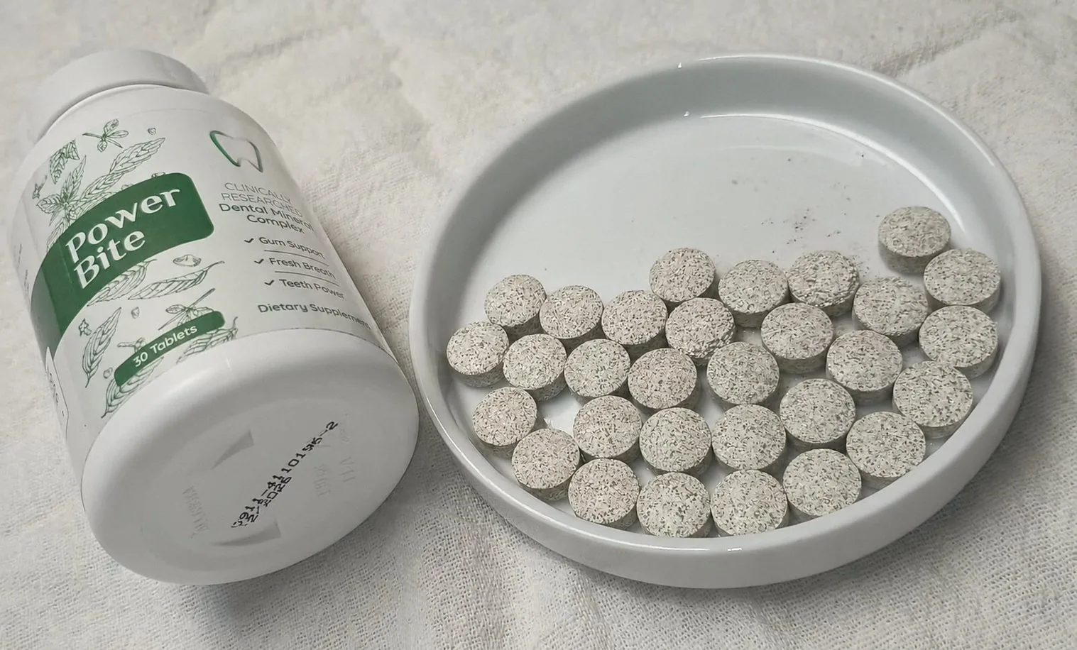 PowerBite bottle on its side beside a white dish holding the full count of speckled beige tablets poured out