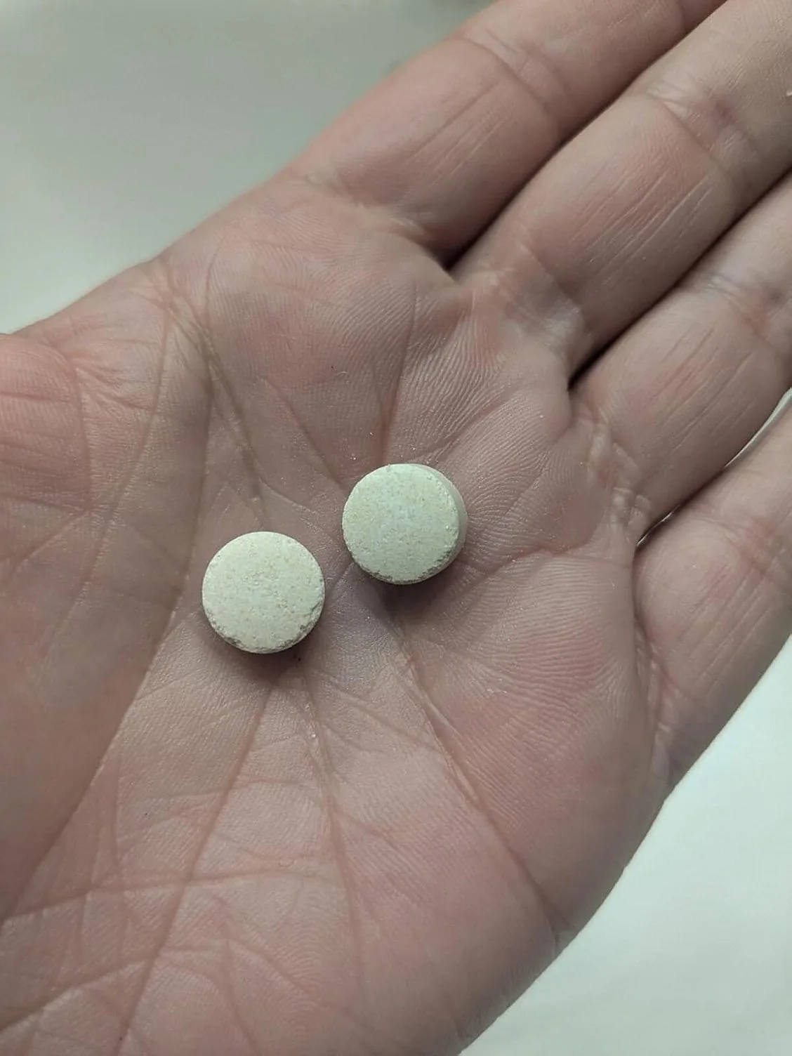 Two cream-colored Synadentix tablets held together in an open palm, showing their speckled, pressed surface