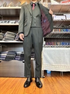 ダークグリーンの深い色合いとメタルボタンが光る、上質なスーツの画像