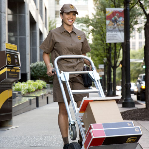 Female UPS driver moving a bunch of boxes on a dolly