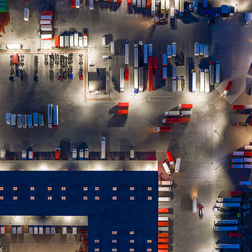 Overhead view of a massive logistics warehouse hub with dozens of semi trucks parked around it.