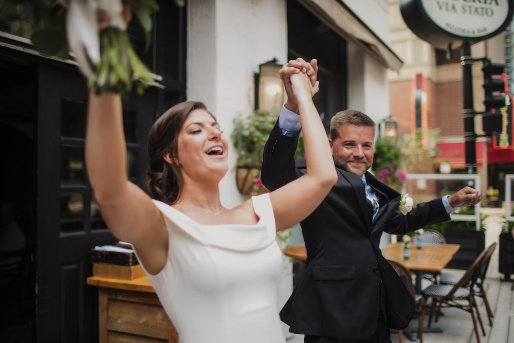 A just married couple cheer after wedding ceremony on outdoor patio of Osteria Via Stato.