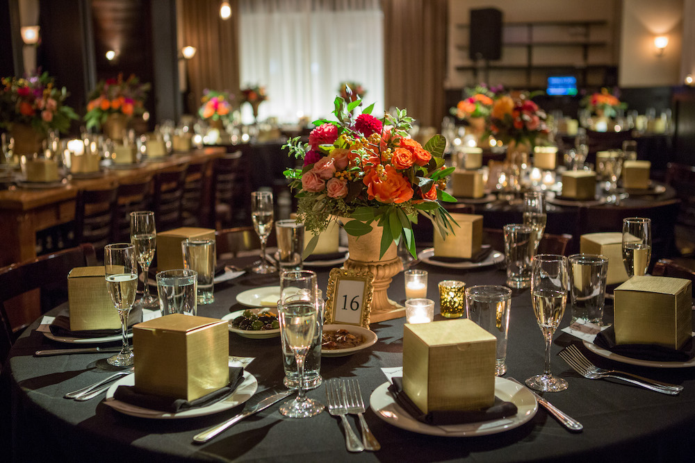 Tables in the dining room are set with floral arrangements and cookie boxes for a wedding reception at Osteria Via Stato.