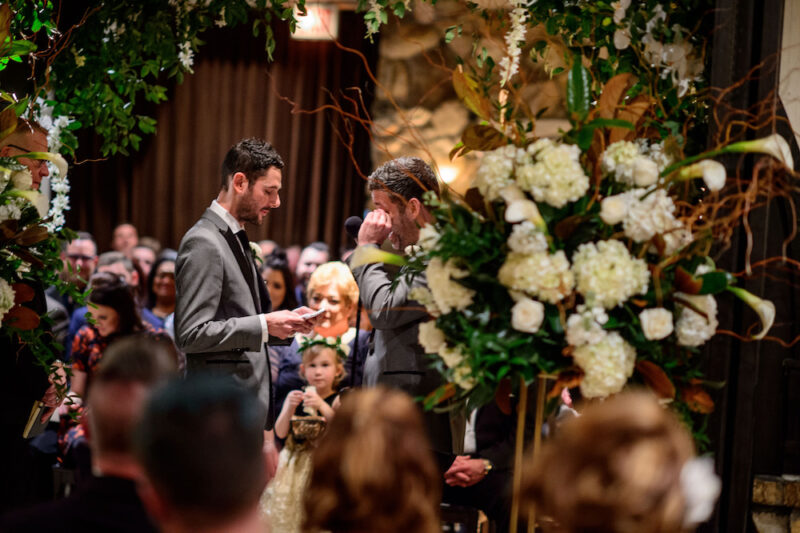 A gay couple gets married under a floral archway at Osteria via Stato.