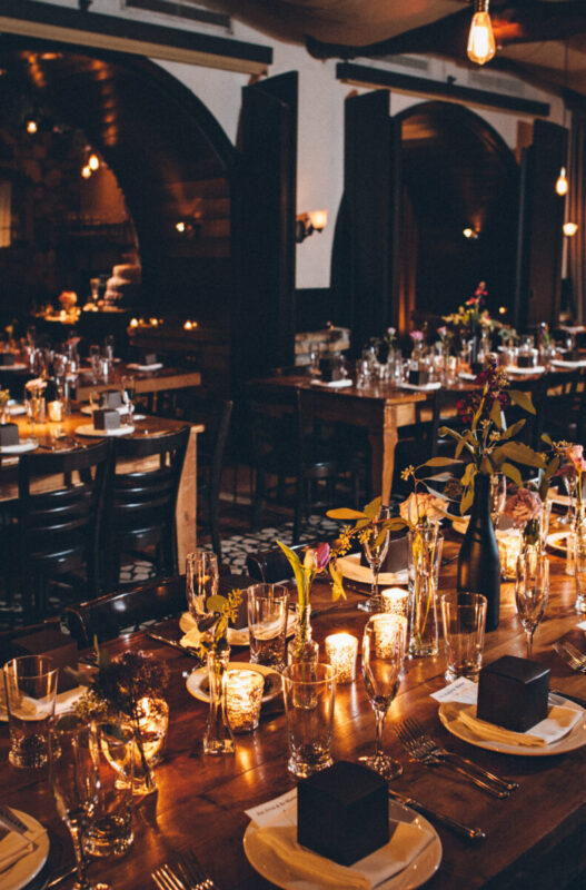 Dinning room tables are set for dinner reception with candles, floral arrangements, and cookie boxes at Osteria Via Stato.