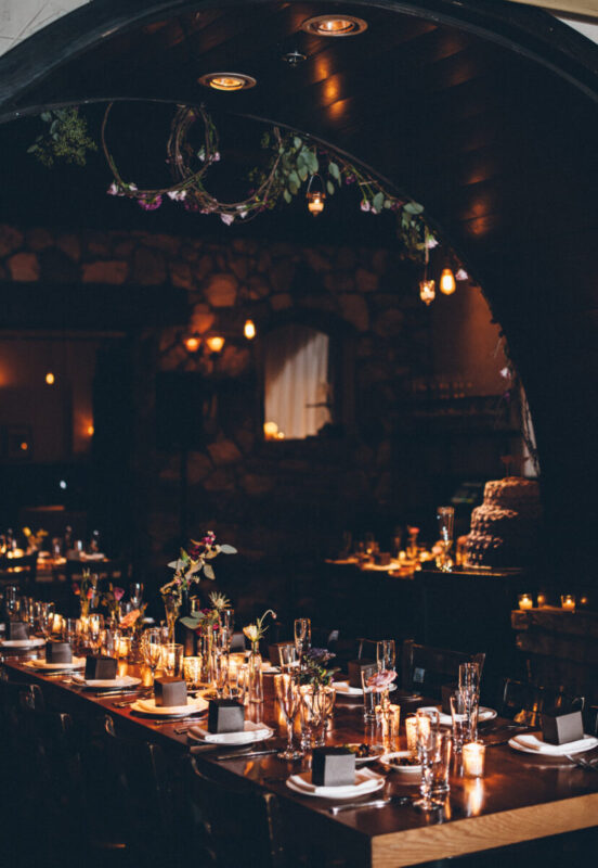 Long wooden table under archway with flowers and candles