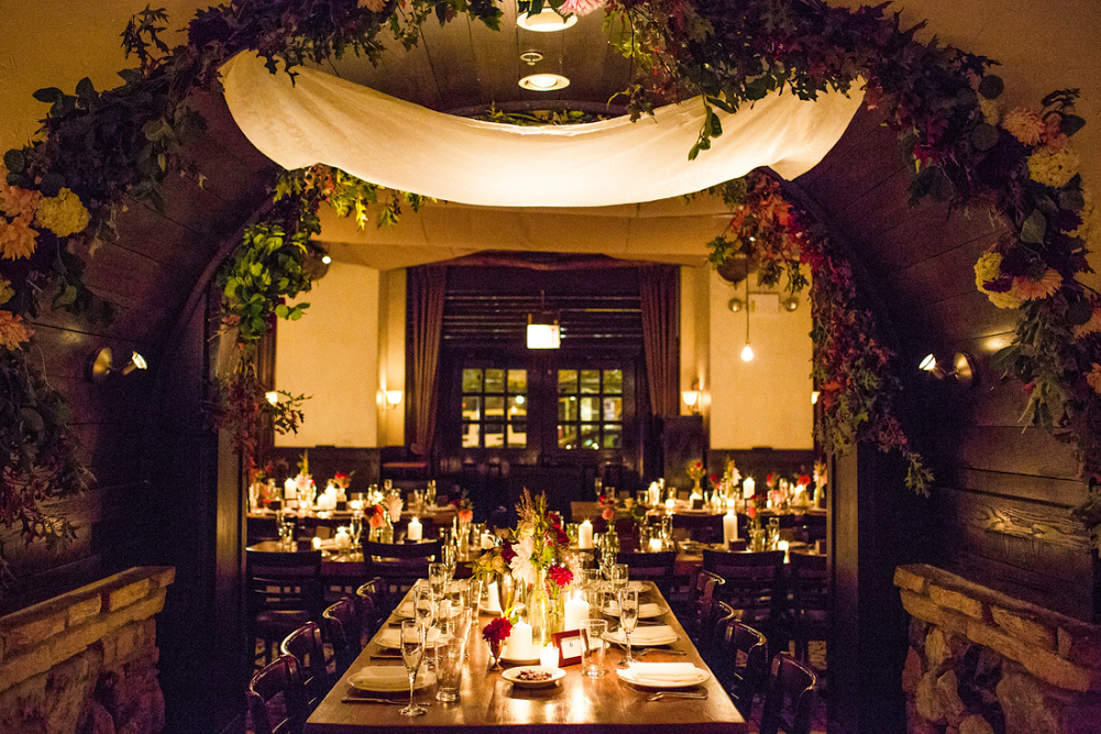 Table is set with candles and floral center pieces for a wedding dinner under floral archway at Osteria via Stato.