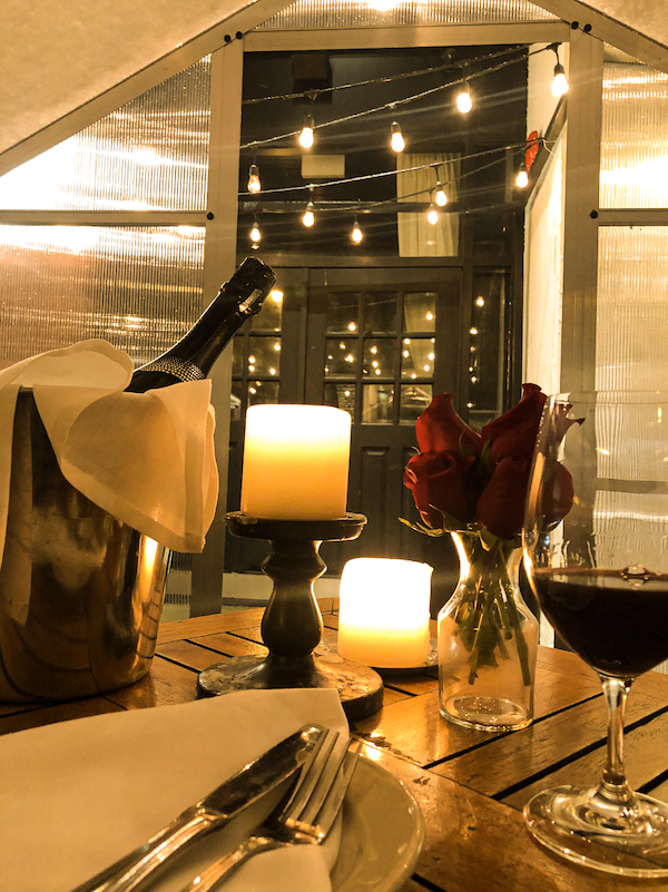 dining table with candles, red roses, wine and bottle of Prosecco in private heated greenhouse at Osteria Via Stato in Chicago.