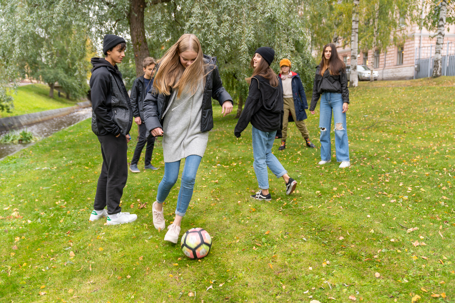 Nuoret pelaavat puistossa jalkapalloa.