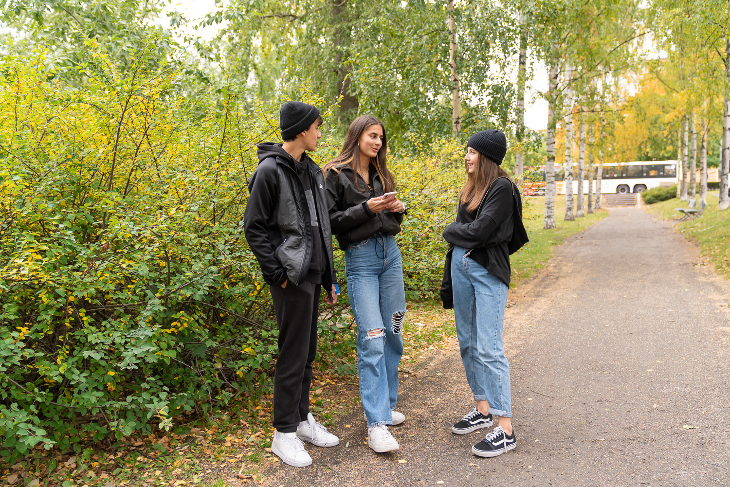 Kolme nuorta henkilöä juttelee puistossa.