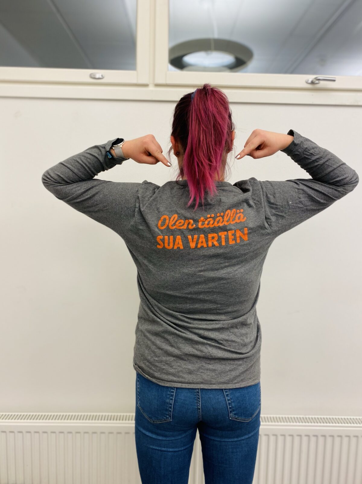 Ohjaaja osoittaa selässä lukevaa "Ole täällä sua varten" -tekstiä