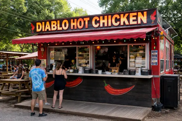 Candid color photo at an outdoor East Austin food park counter: a staff member wearing gloves is ...