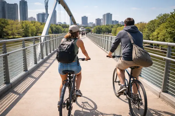 Candid daytime photograph of two cyclists — a woman and her partner — riding side-by-side across ...