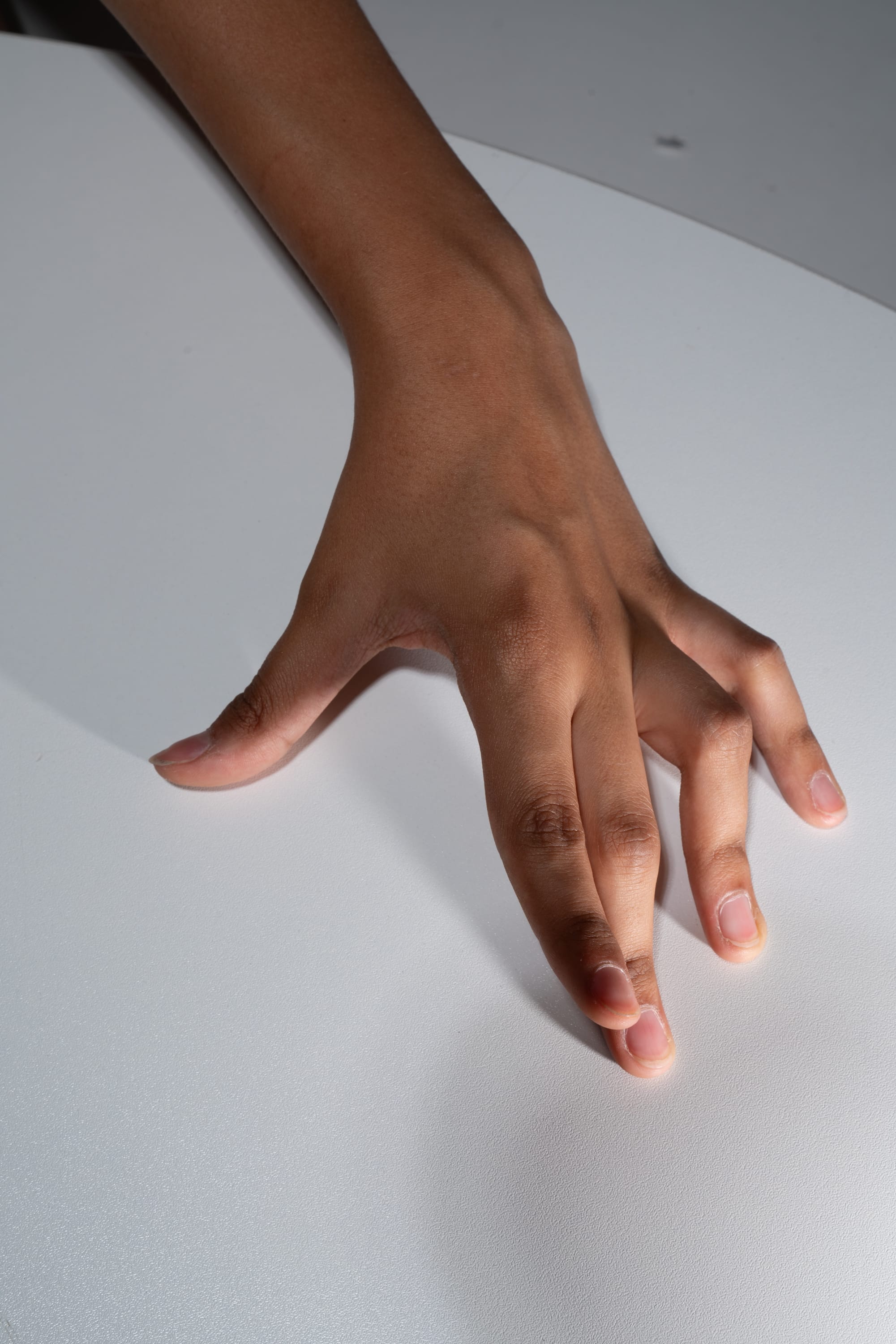 a hand with brown skin is resting on a white textured surface. the fingers are spread out and the thumb is touching the index finger. the lighting is soft and the image is a closeup.