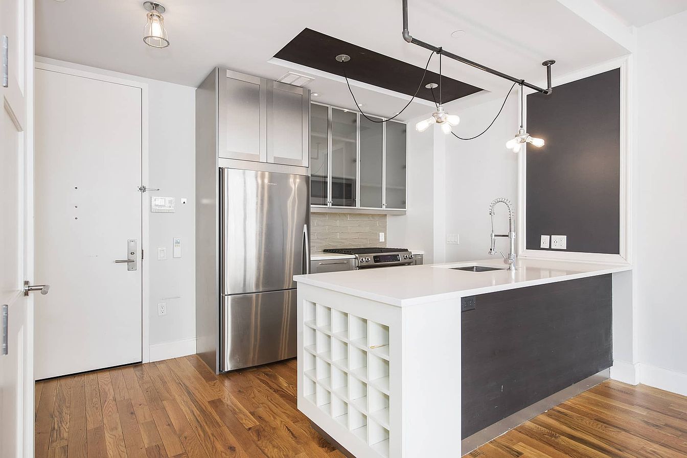 a modern kitchen with stainless steel appliances and white cabinets. the kitchen has an island with a white countertop and a gray base. there is a sink and faucet on the island. the kitchen also has hardwood floors. the kitchen is open to the living room.