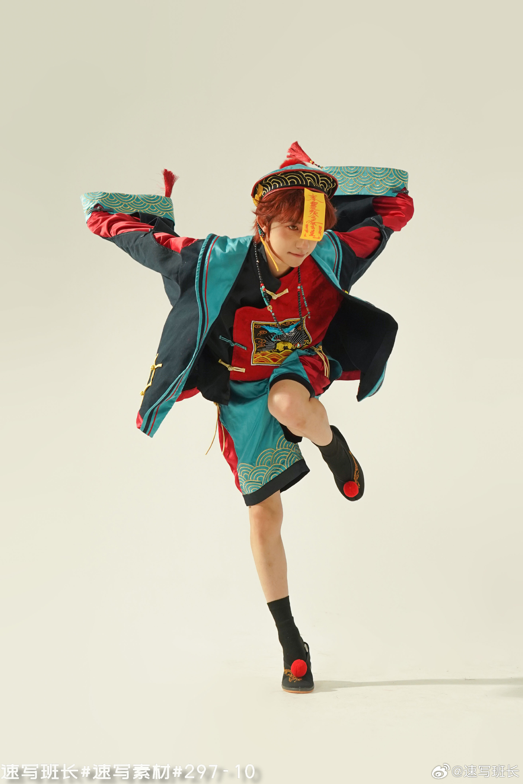 a young man strikes a dynamic pose, dressed in a vibrant costume inspired by traditional chinese opera. the costume features a striking combination of red, blue, and yellow, with intricate embroidery and patterns. he wears a black hat with a yellow inscription. the background is a clean white, emphasizing the performer and his colorful attire. the image captures the energy and drama of his performance.