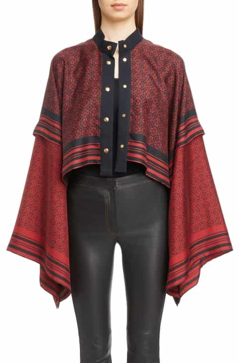a woman wearing a patterned red and black blouse with gold buttons and black highwaisted pants.