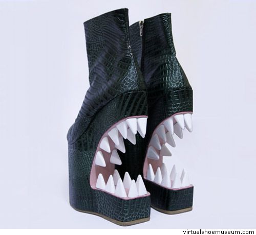 this image shows a pair of green, black, and white highheeled boots with a platform wedge base. the most distinctive feature of the shoes is their front, which is shaped like a wideopen mouth with sharp white teeth. the shoes are stylish and unique, with a creative and artistic design. the abstract and whimsical nature of the design suggests a playful and eccentric approach to fashion.