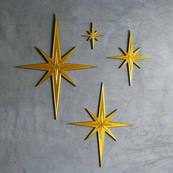 four gold stars are arranged on a grey wall.  the stars are different sizes and have points that extend outward from the center.  they are all in a vintage style.  the wall is rough and textured, with subtle streaks and patterns.  the stars are welllit and appear shiny.