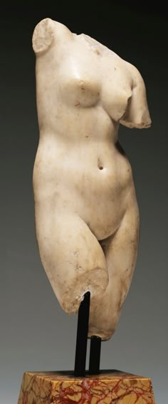 this is a closeup photo of a marble statue of a female torso. the statue is carved in a classic style, with the woman's body depicted in a naturalistic and graceful pose. the marble is white and polished, giving the statue a smooth and elegant appearance. the statue is displayed on a marble base and the image is shot from an angle that highlights the curves of the female form. the statue is a beautiful example of ancient art and is a reminder of the skill and artistry of the people who created it. it's also a testament to the enduring beauty of the human form.