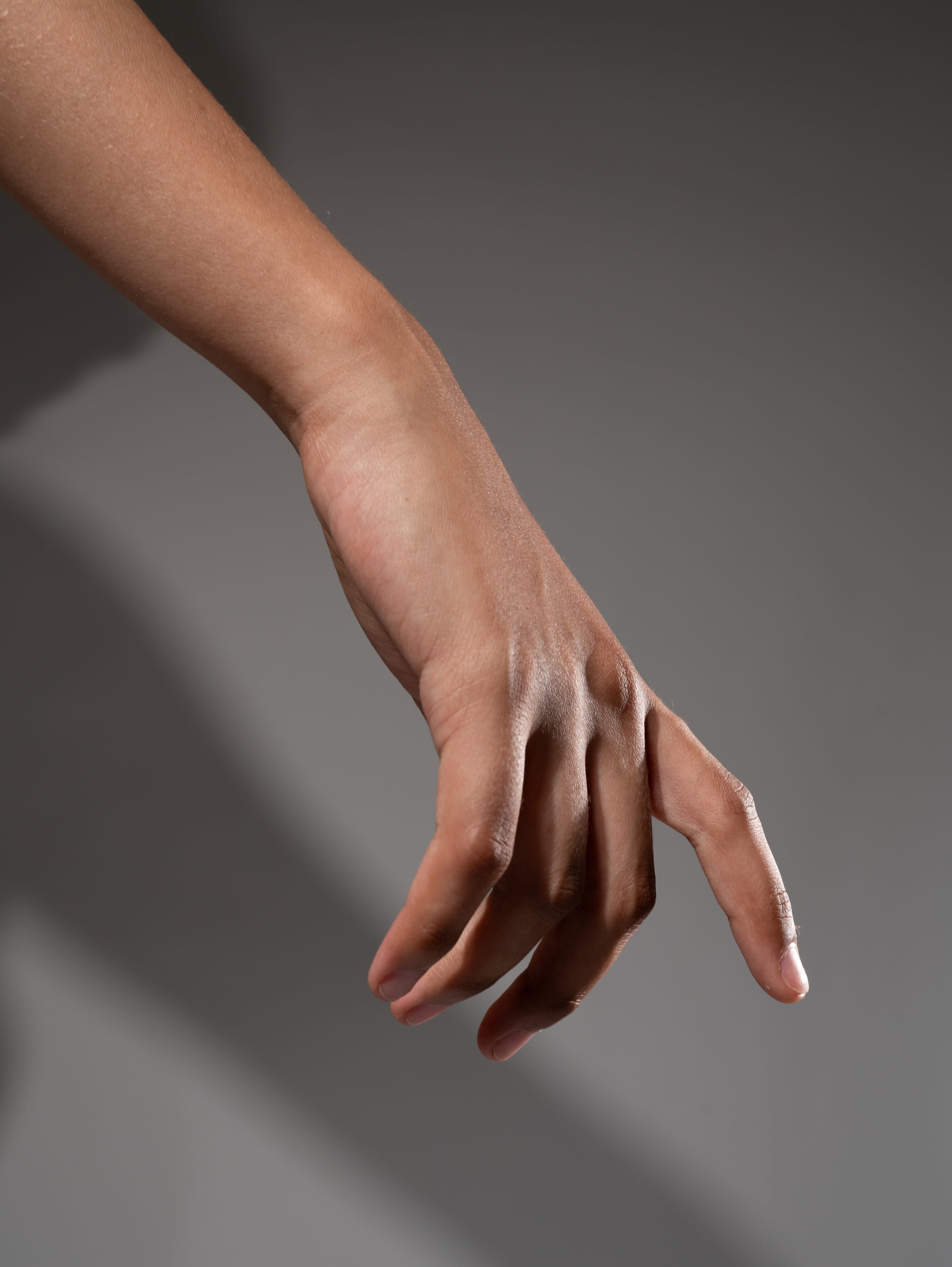 a moderately tanned hand is reaching downward with the fingers curled in a gesture of grasping. the arm and hand are illuminated by studio lighting.