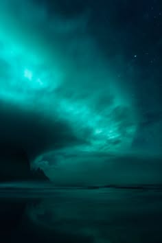 a stunning view of the aurora borealis, or northern lights, painting the night sky with vibrant green and blue hues. the celestial display is reflected in the calm, dark waters of the ocean, creating a mesmerizing and peaceful scene. the clouds seem to be flowing and dancing with the lights, creating a magical and otherworldly atmosphere. the image is a testament to the beauty and wonder of nature.