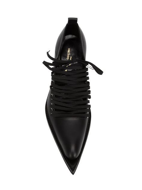 a studio shot of a pair of women's black leather pointedtoe shoes with laceup detailing. the shoes are from the brand comme des garçons and have a sleek, elegant design.  they appear to be ankle boots or booties with a sharp pointed toe and are shown against a clean white background.