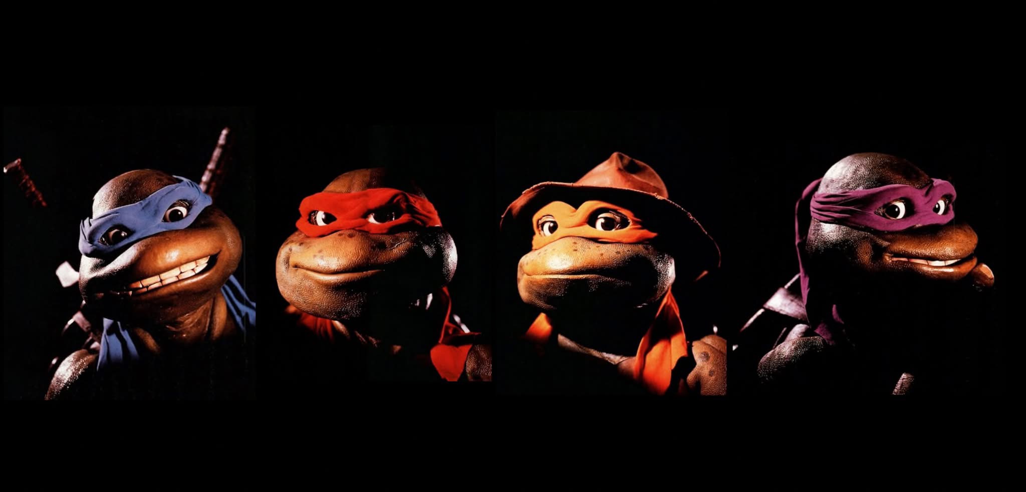 the image shows the four teenage mutant ninja turtles: leonardo, raphael, michelangelo, and donatello. they are depicted as they appeared in the 1990 liveaction movie, with detailed costumes and masks representing each character's signature color and weapon. the background is black.