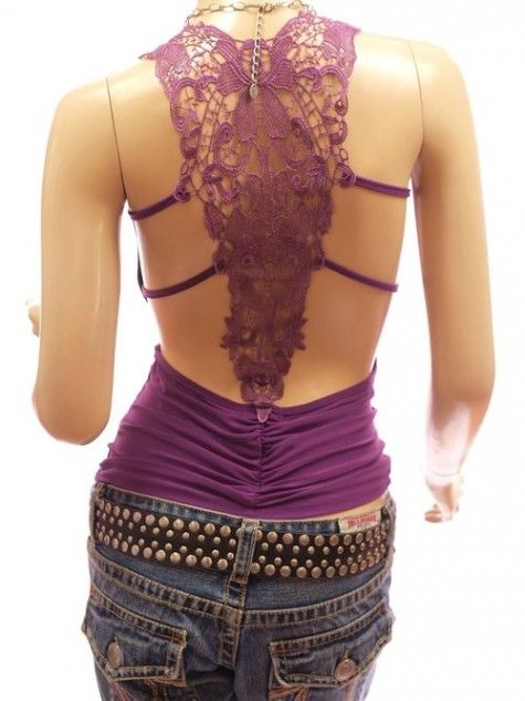 a woman is wearing a purple lace top with crisscross straps in the back. she is wearing blue jeans with a studded belt. the top is backless and the lace is visible from the back. the woman is looking away from the camera.