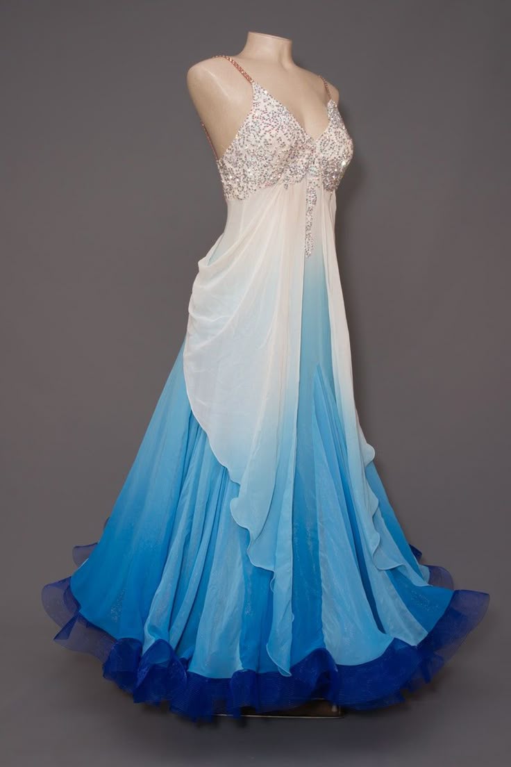 a mannequin displays a floorlength gown in ombre shades of blue and white. the bodice is strapless and heavily beaded, transitioning into a flowing chiffon skirt that begins white and fades into various shades of blue towards the hem. the hem is finished with a darker blue trim. the gown is sleeveless.