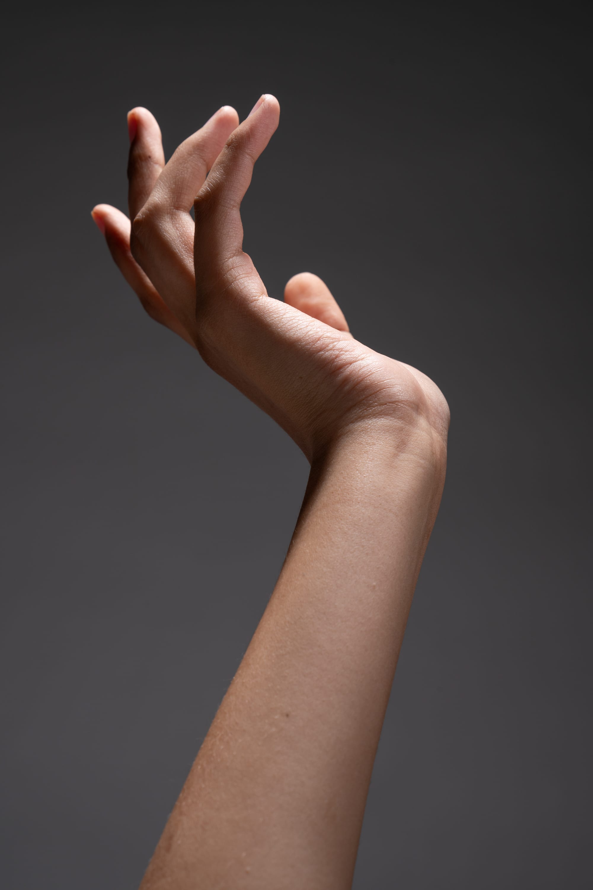 a woman's arm extended upwards, with her hand delicately posed against a dark gray background. the lighting emphasizes the smooth contours of her skin, creating a sense of elegance and artistry.