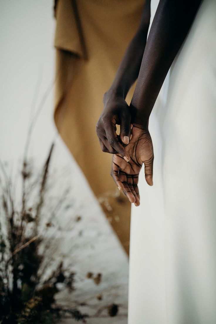 a close up image of a woman's hand and arm holding a white dress. the skin is black and the dress is white. the background is blurred and out of focus. the image is minimalist and elegant.
